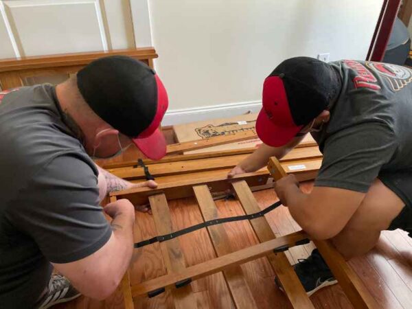Two men assembling wooden bed frame indoors.