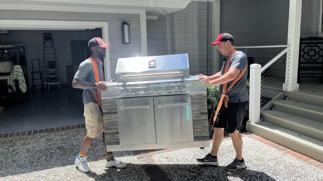 Two people moving a stainless steel outdoor grill.
