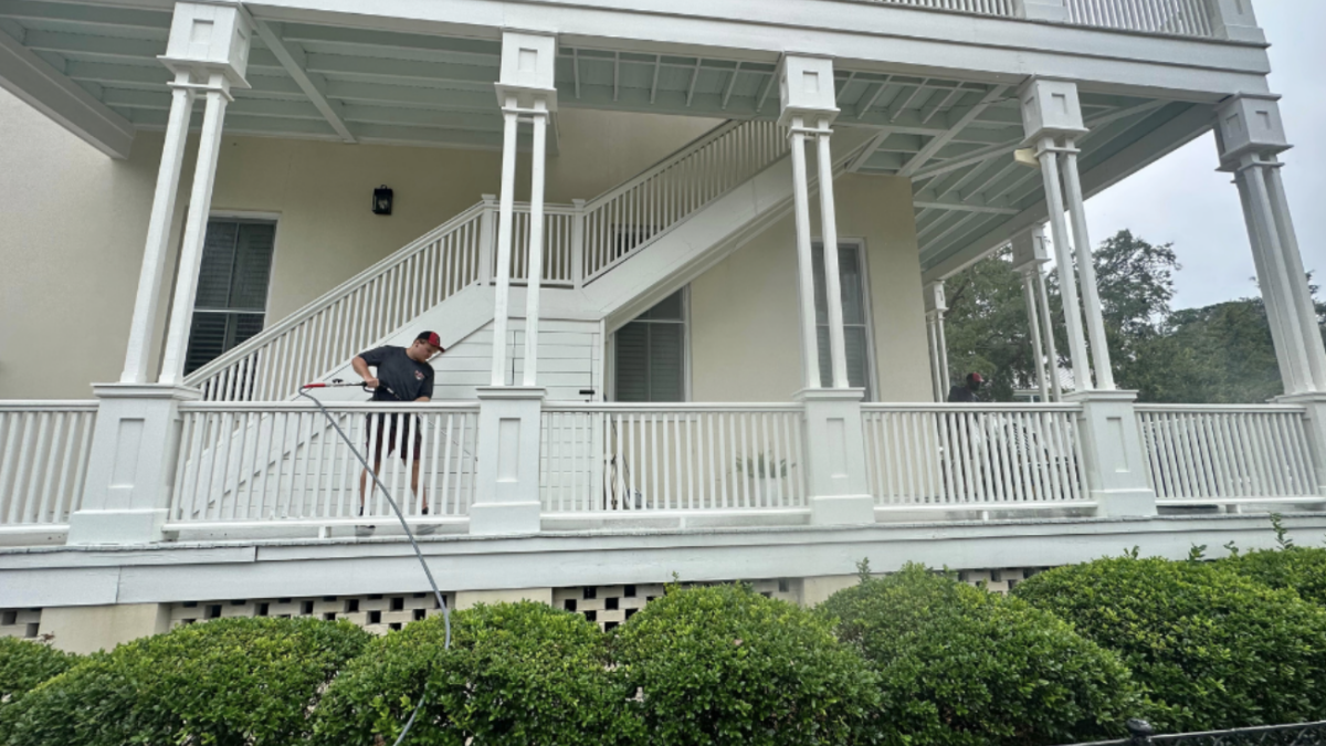 Person pressure washing a house balcony