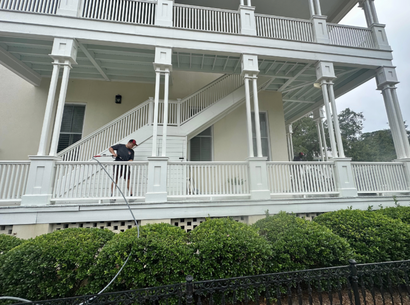 Person pressure washing a house balcony