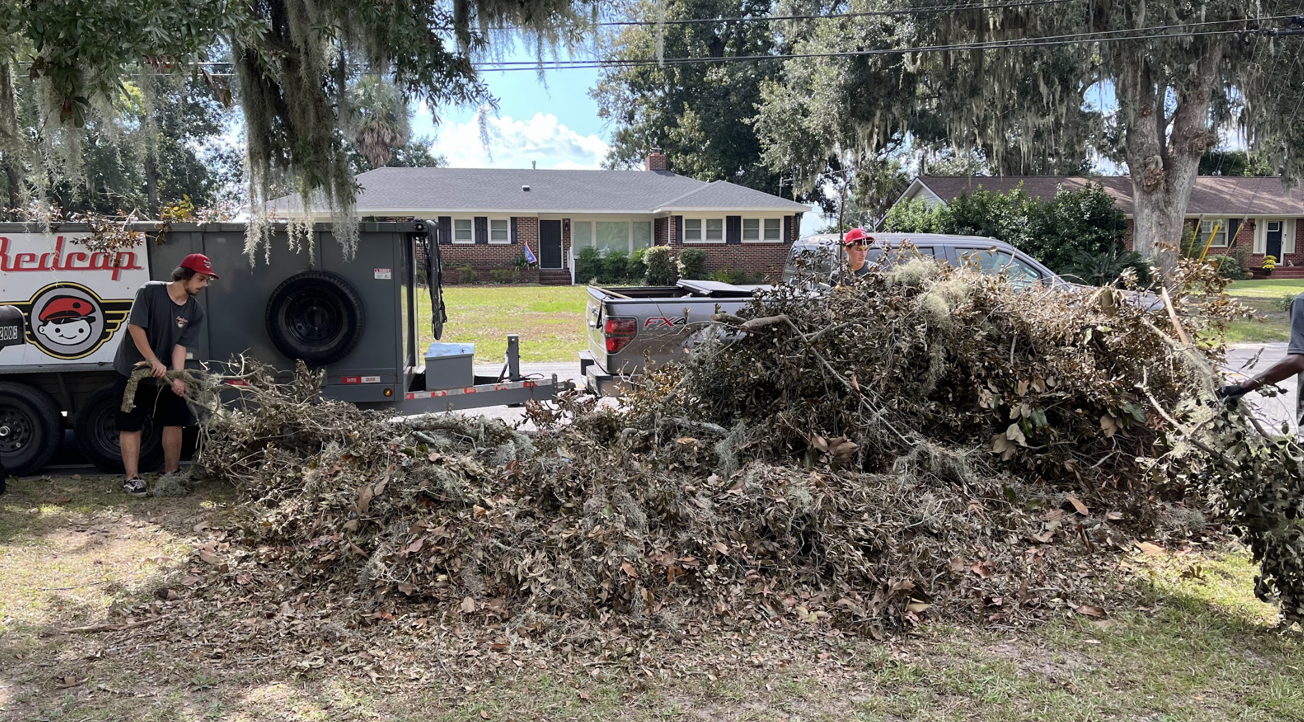 Workers clearing yard debris with truck and trailer.