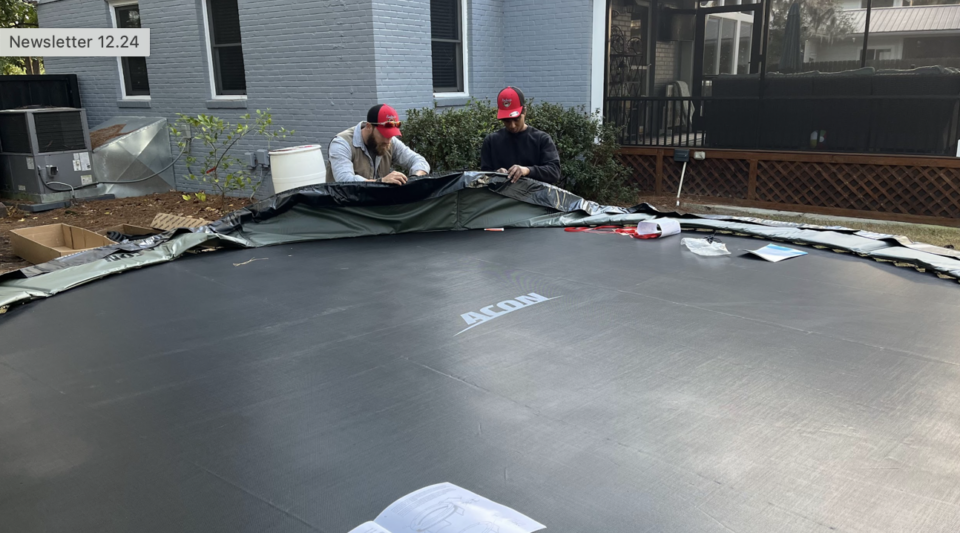 Two people assembling a large trampoline outside.
