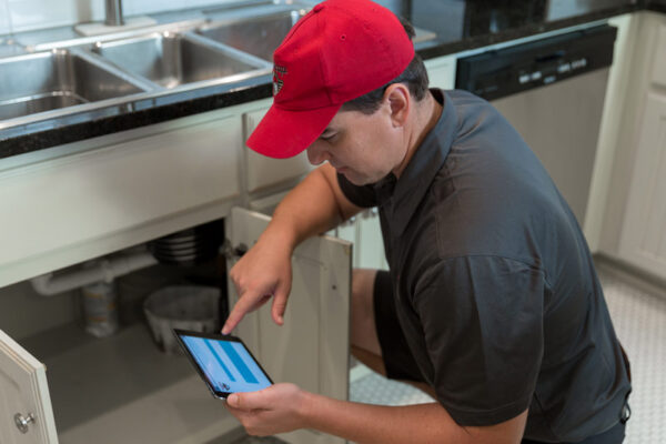 Plumber inspecting under sink with a tablet