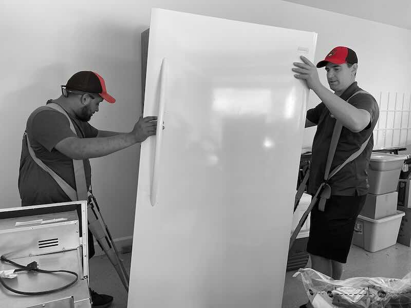 Two movers handling large refrigerator with straps.
