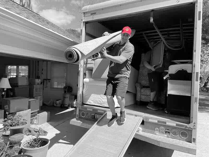 Man unloading rolled carpet from moving truck